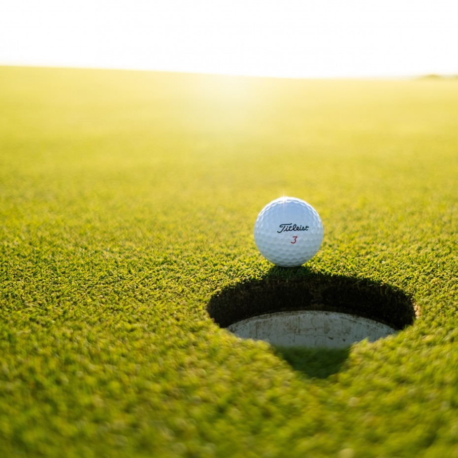 Golfball liegt am Loch in der Sonne