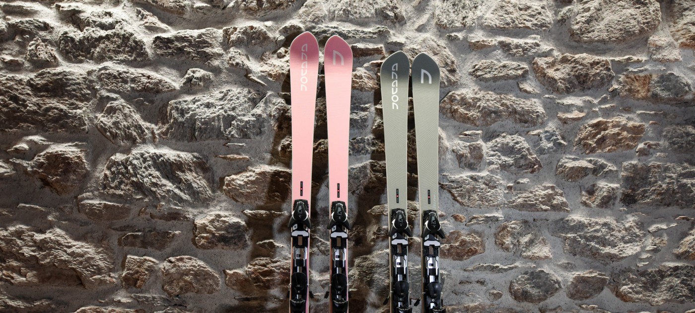 Rosa und Graue Skier lehnen an einer Steinwand
